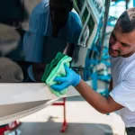 Boat maintenance - A man cleaning boat with cloth.